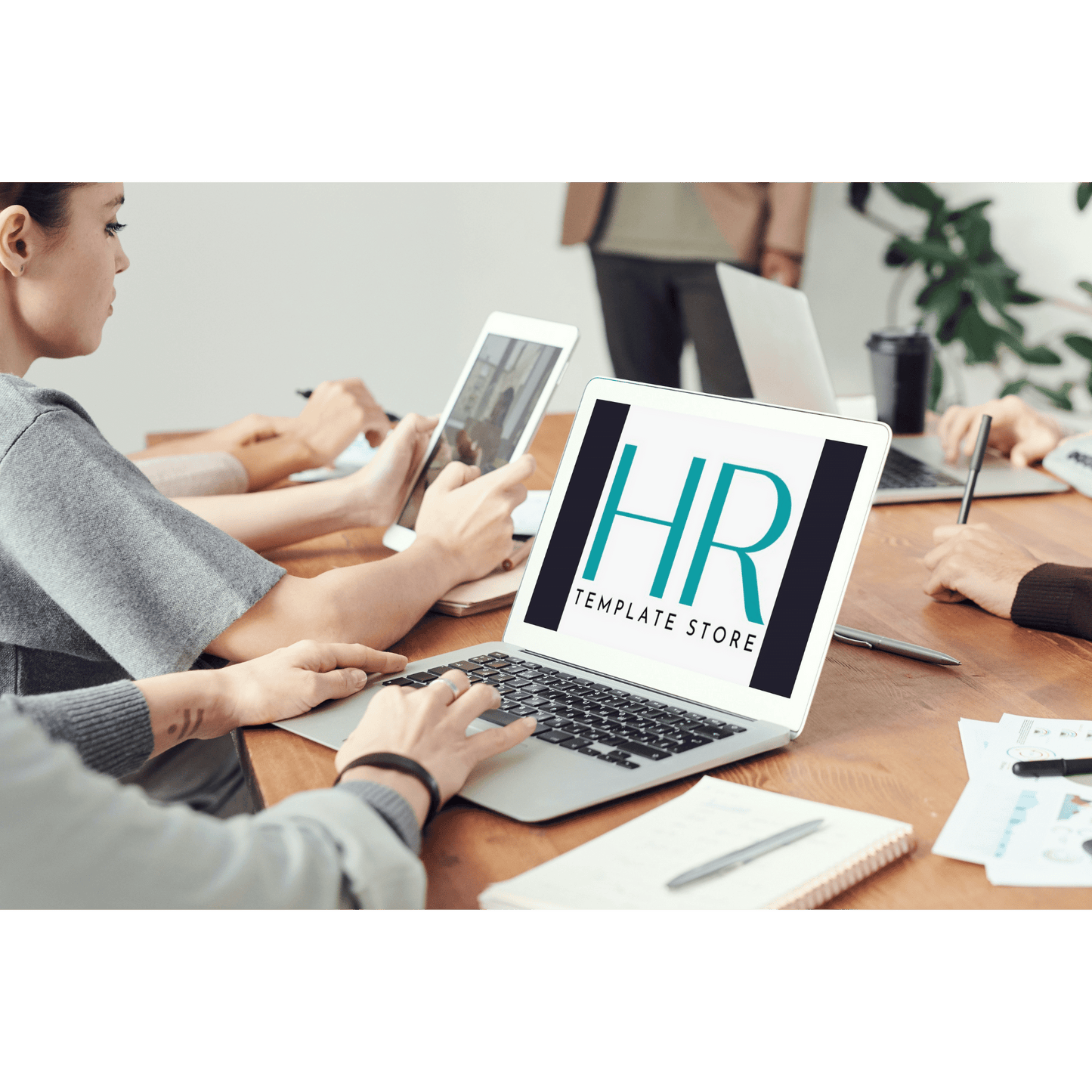 The HR Template Store logo displayed on a laptop placed on a busy team workspace..