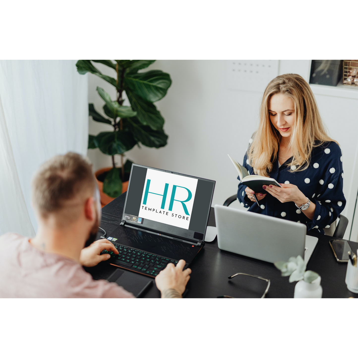 A man viewing the HR Template Store logo displayed on a laptop placed on a tidy and organized desktop. A woman sits across from him, reading from a notebook.