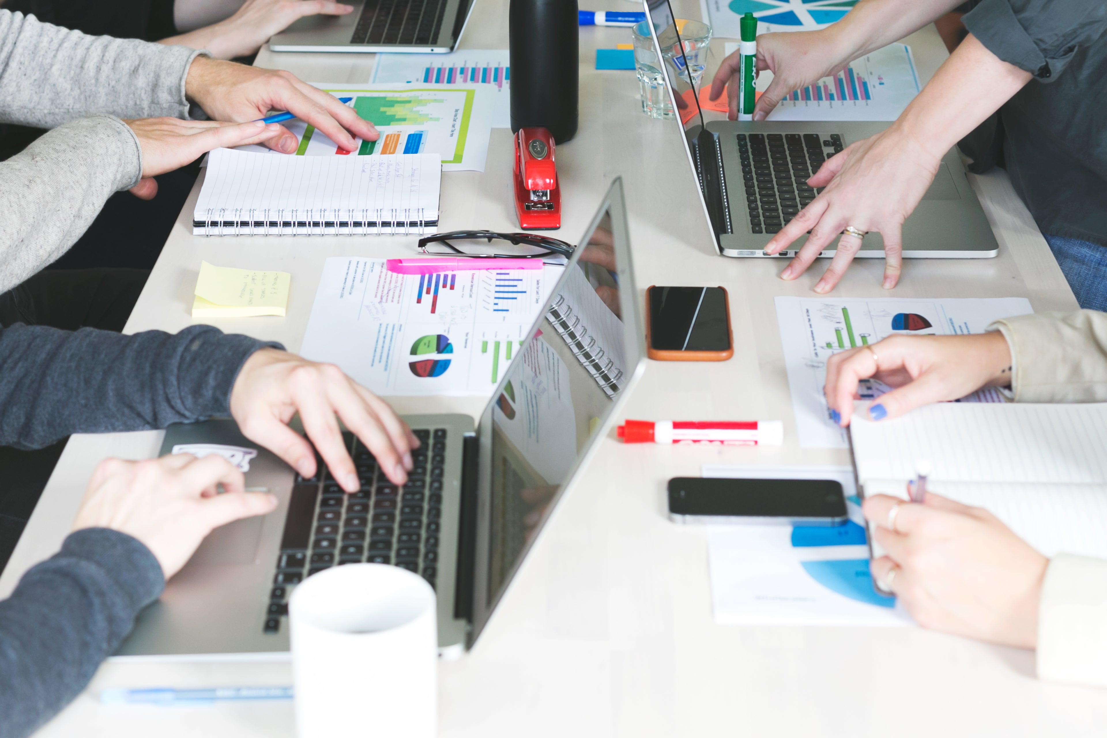 A crowded conference table in a professional setting showing laptops, sales charts, and notebooks