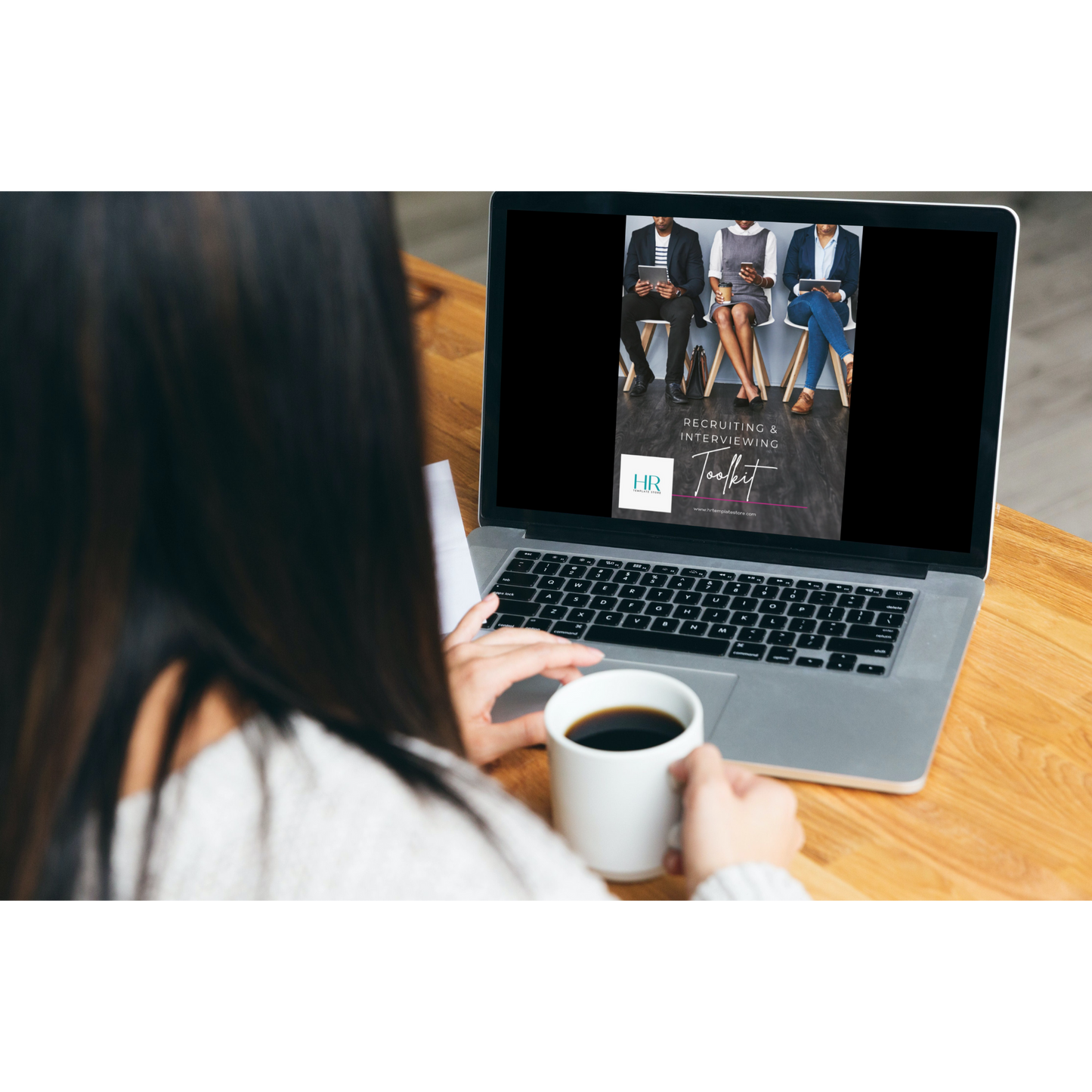 Women holding a cup of coffee while looking at her laptop that displays a picture of our Recruiting and Interviewing toolkit cover page. 